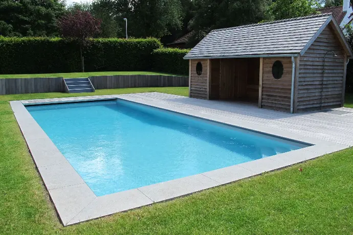 Piscine rectangulaire en béton avec margelles grises et pool house en bois – Réalisation haut de gamme Le Petit Baigneur