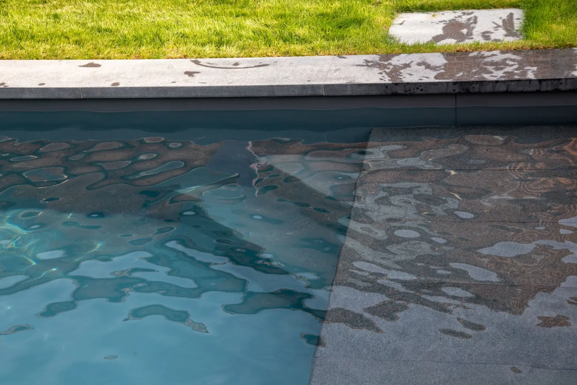 Piscine design avec reflets sur l’eau et margelles grises — Le Petit Baigneur